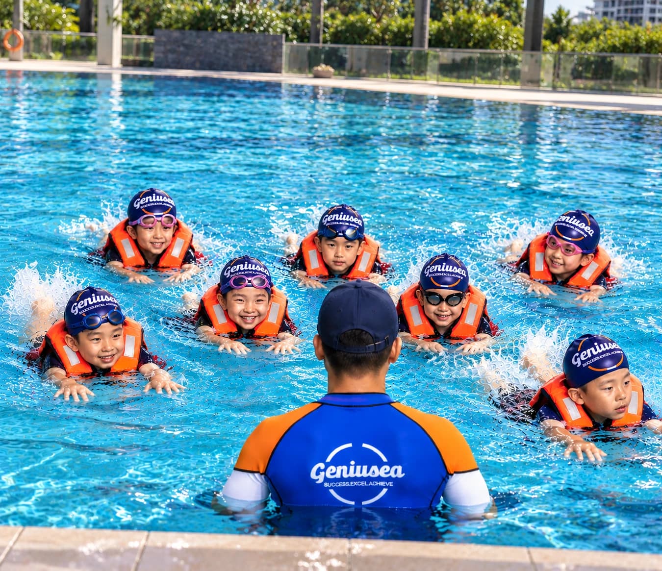 Geniusea coach teaching a group of smiling kids in Geniusea swim caps and orange vests