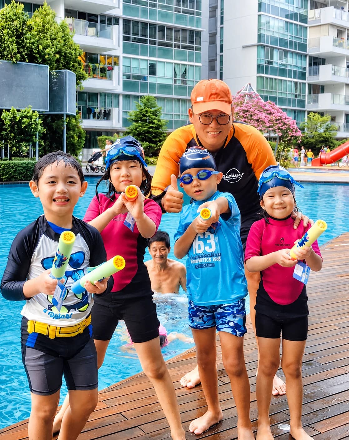 Coach in an orange cap with four kids holding water guns by a condo pool