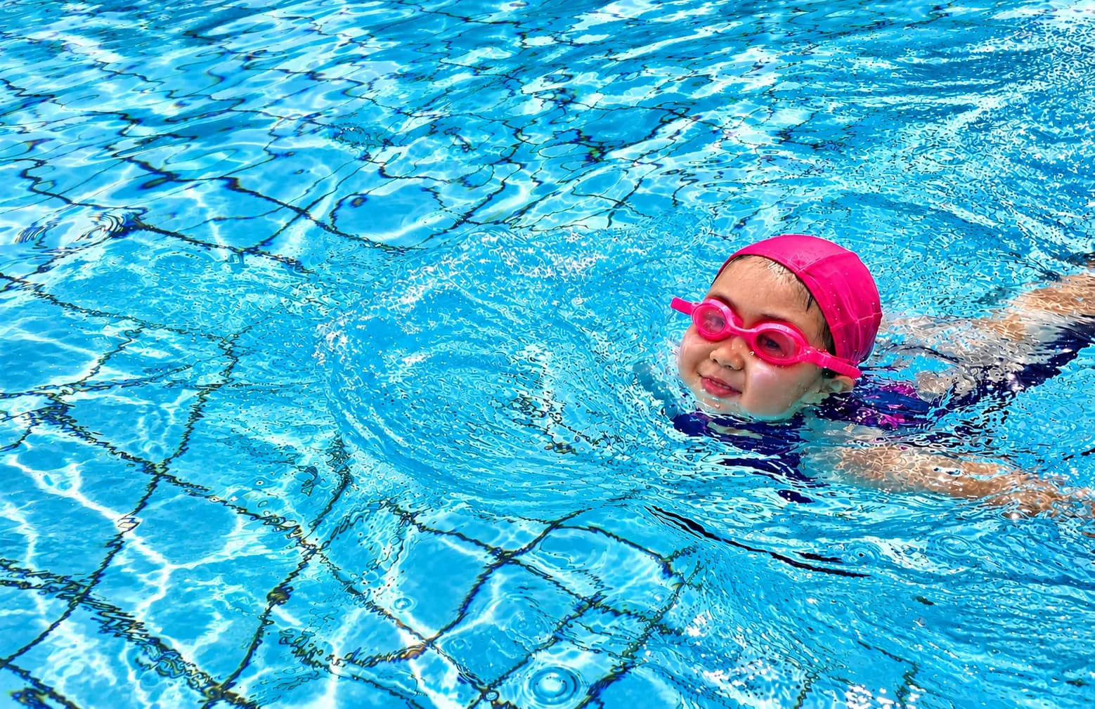 Girl in a pink cap and goggles swimming with a smile