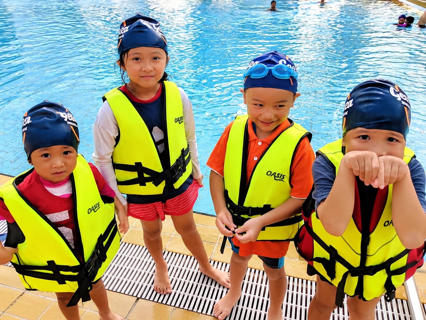 Four kids in life jackets and Geniusea caps by the pool