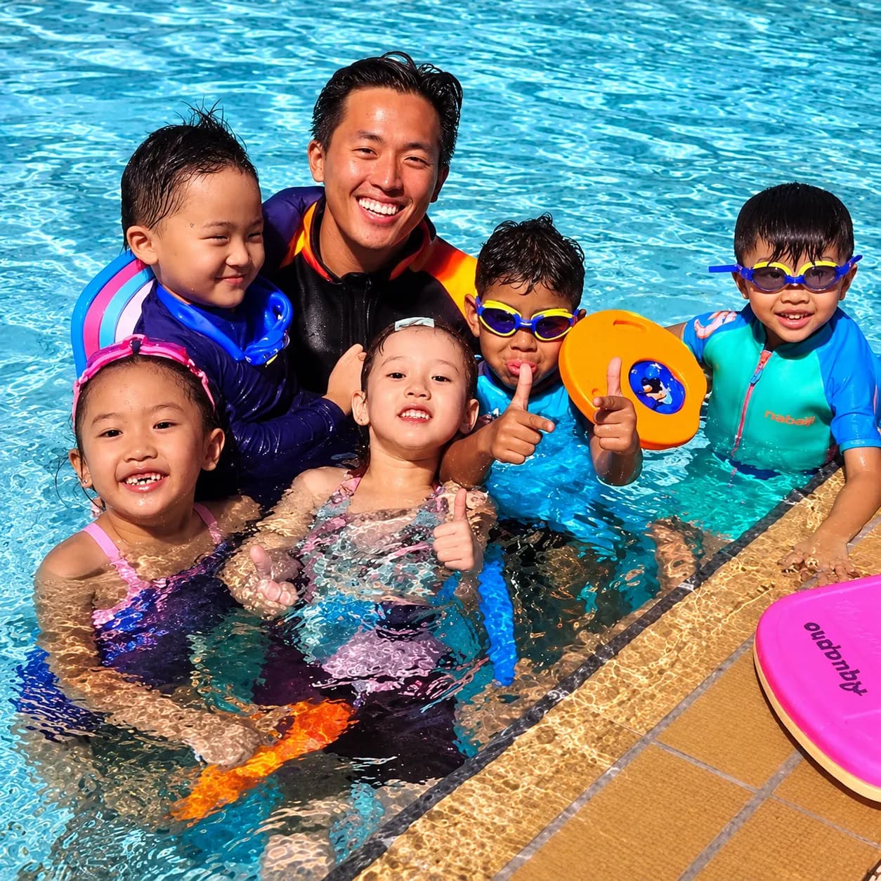 Coach with smiling young swimmers giving thumbs up in the pool
